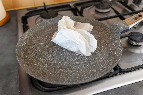 Spreading oil over the surface of the frying pan with a paper kitchen towel