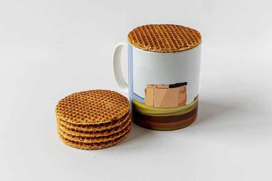A stroopwafel on a mug of coffee beside a stack of stroopwafels
