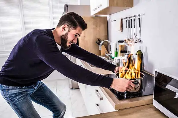 A man trying to lift a pan that is on fire