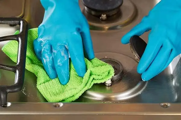 Cleaning a stovetop wearing rubber gloves